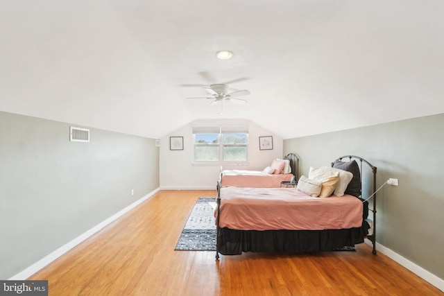 bedroom with a ceiling fan, visible vents, baseboards, vaulted ceiling, and light wood-style floors