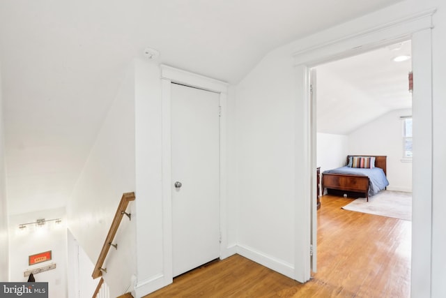 hall with an upstairs landing, lofted ceiling, and light wood-style flooring