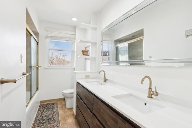 full bath with double vanity, combined bath / shower with glass door, toilet, and a sink