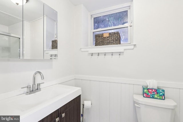 bathroom featuring an enclosed shower, vanity, toilet, and wainscoting