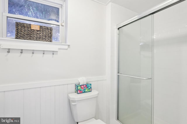 bathroom featuring toilet, a stall shower, and wainscoting