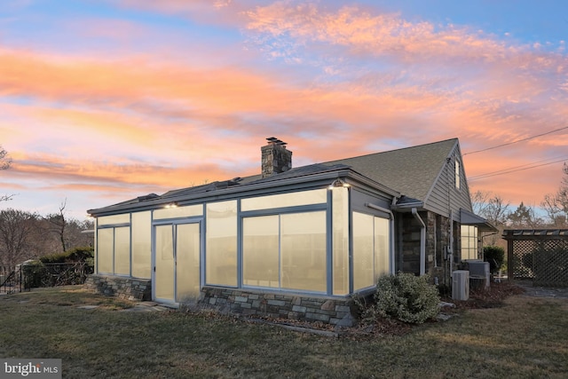 back of house featuring cooling unit, roof with shingles, a yard, a chimney, and stone siding