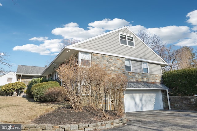 view of home's exterior with aphalt driveway, stone siding, and a garage