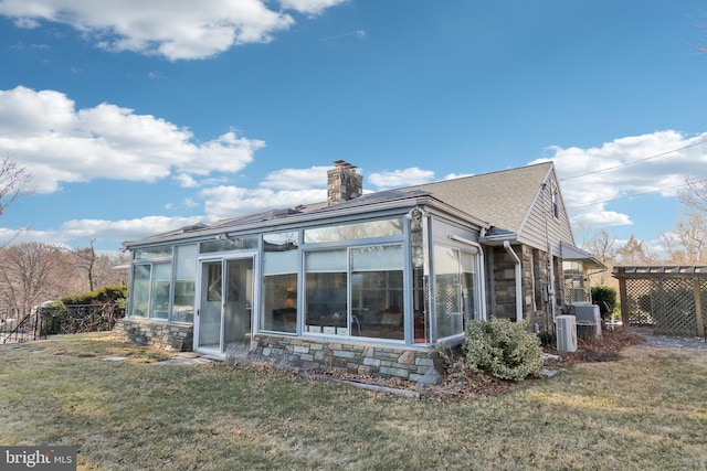 back of property featuring stone siding, a lawn, a chimney, and a sunroom