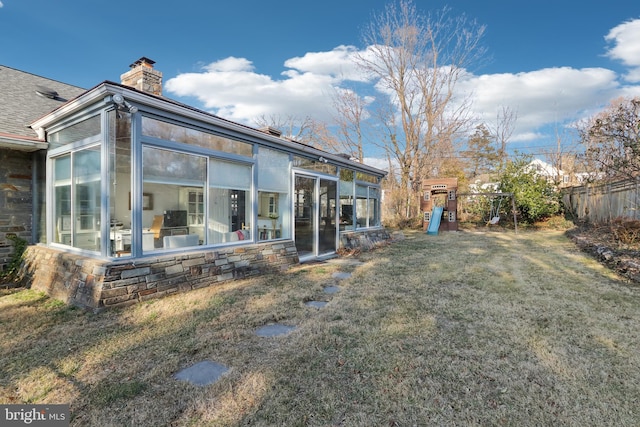 back of house featuring a playground, fence, a chimney, a yard, and a sunroom