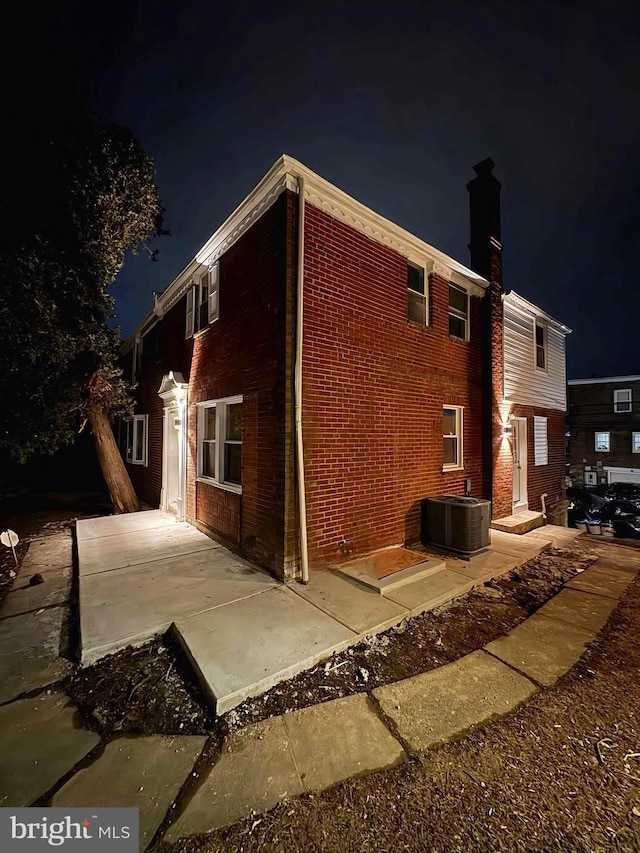 property exterior at night with cooling unit, a patio area, and brick siding