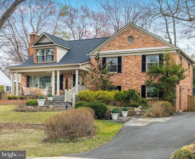 view of front of house with a shingled roof, covered porch, brick siding, and a chimney