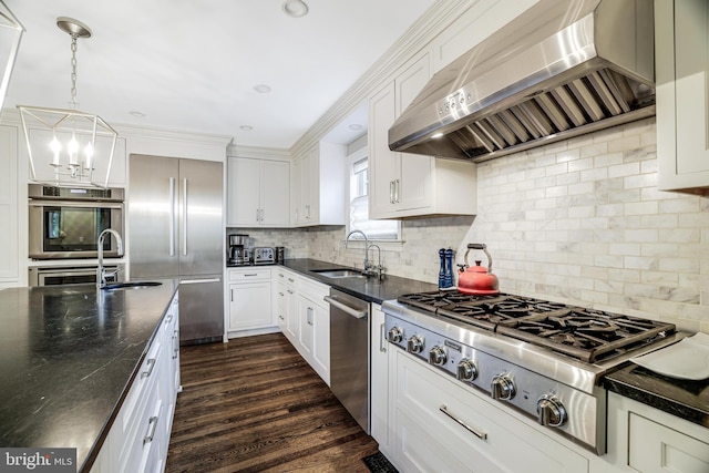 kitchen with dark wood-type flooring, a sink, stainless steel appliances, an inviting chandelier, and wall chimney range hood