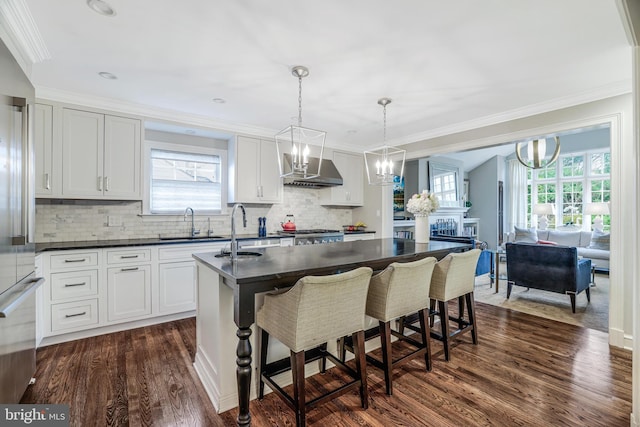 kitchen with a sink, dark wood-type flooring, dark countertops, and wall chimney range hood