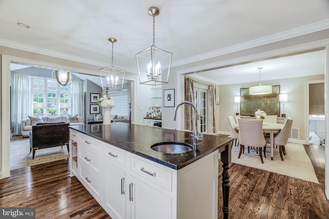 kitchen with dark wood finished floors, dark stone countertops, a center island with sink, and a sink