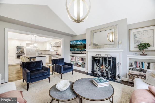 living room featuring baseboards, a chandelier, a fireplace with flush hearth, light wood-style floors, and high vaulted ceiling