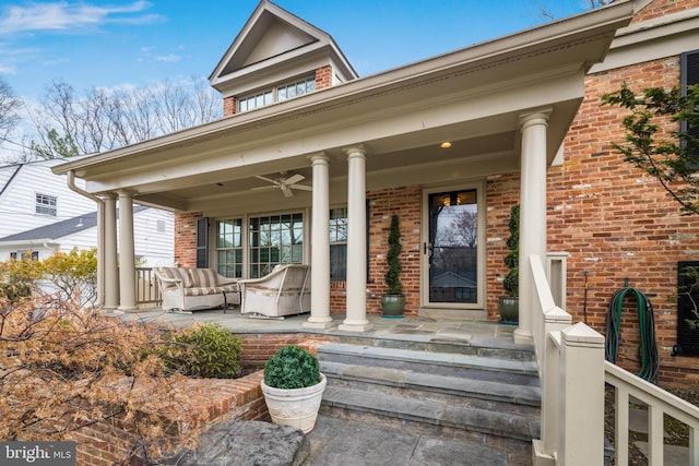 view of exterior entry featuring brick siding, a porch, and a ceiling fan