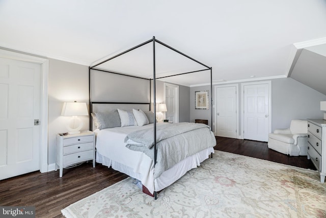 bedroom with wood finished floors, lofted ceiling, ornamental molding, and multiple closets