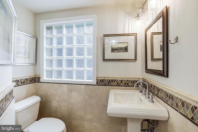 bathroom featuring a wainscoted wall, toilet, tile walls, and a sink