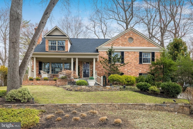 view of front of house featuring brick siding, a front yard, roof with shingles, covered porch, and a ceiling fan