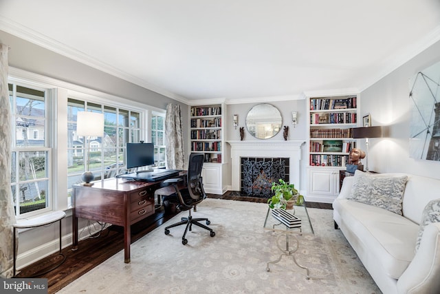 office space featuring built in shelves, baseboards, ornamental molding, a tile fireplace, and wood finished floors