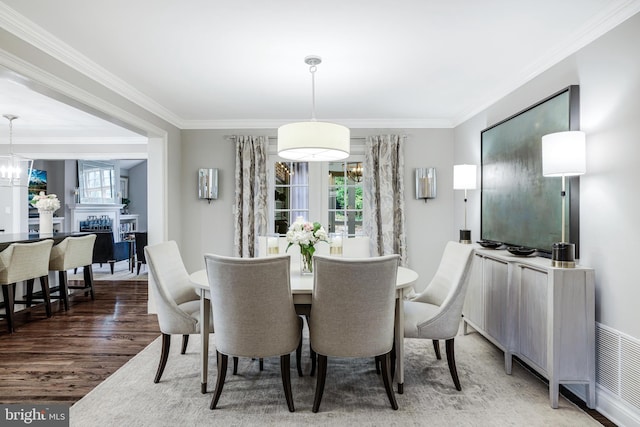 dining room featuring a fireplace, crown molding, wood finished floors, and a chandelier