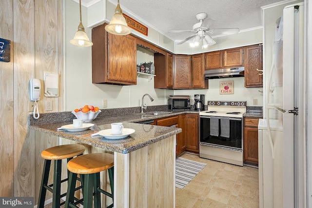 kitchen with brown cabinets, a sink, a peninsula, white appliances, and under cabinet range hood
