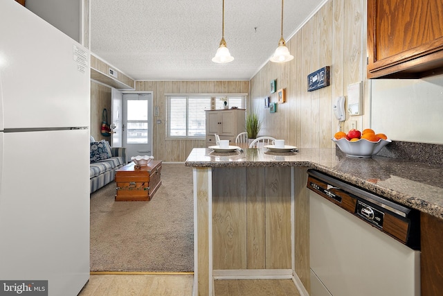 kitchen with a textured ceiling, a peninsula, white appliances, carpet flooring, and dark stone countertops