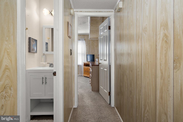 corridor featuring carpet flooring, a sink, wooden walls, and a textured ceiling