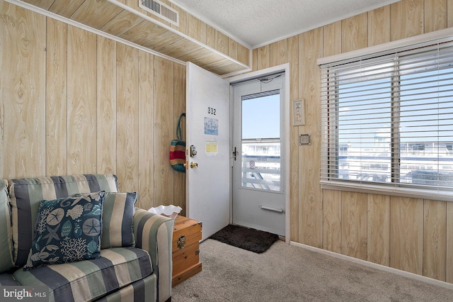 entryway featuring carpet, visible vents, wood walls, and a textured ceiling