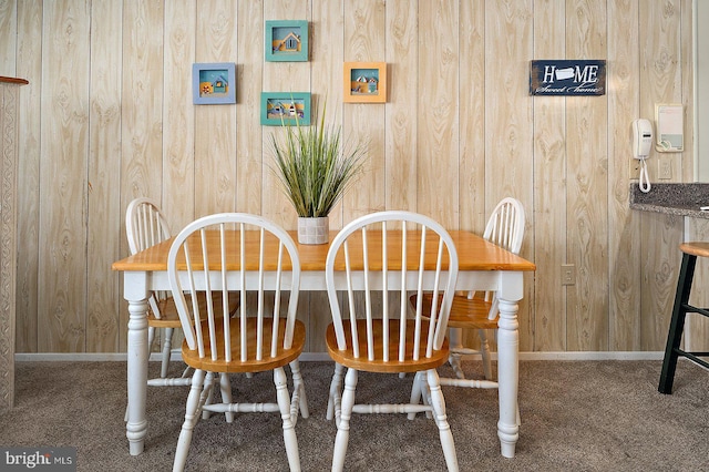 carpeted dining room with wood walls and baseboards