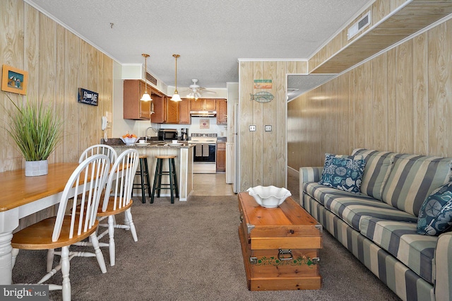 living area featuring a textured ceiling, light colored carpet, wood walls, a ceiling fan, and crown molding