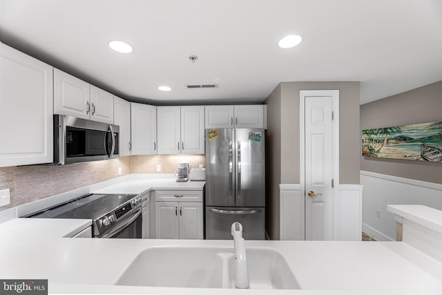 kitchen with visible vents, a wainscoted wall, stainless steel appliances, light countertops, and white cabinetry