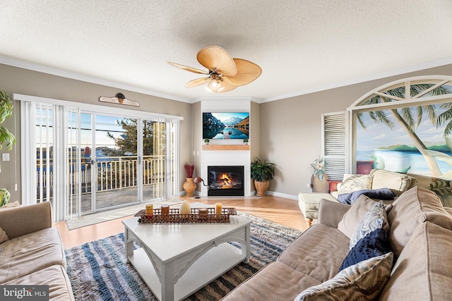 living area with a textured ceiling, a fireplace with flush hearth, wood finished floors, a ceiling fan, and crown molding