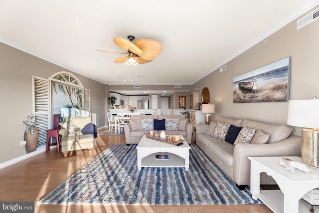 living area featuring a ceiling fan, visible vents, crown molding, and wood finished floors