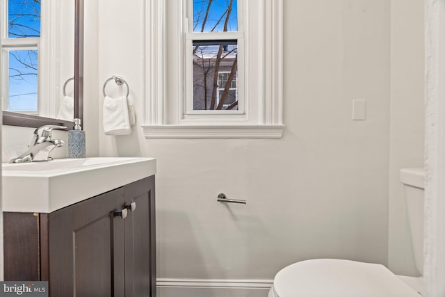 half bathroom with toilet, a healthy amount of sunlight, baseboards, and vanity