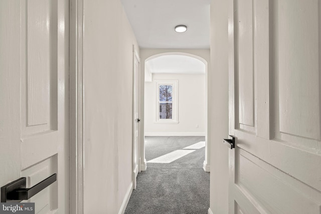 hallway with arched walkways, carpet flooring, and baseboards