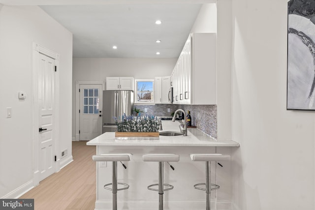 kitchen featuring white cabinets, freestanding refrigerator, a sink, a kitchen bar, and backsplash