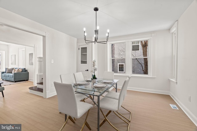 dining space with baseboards, light wood-type flooring, visible vents, and a notable chandelier