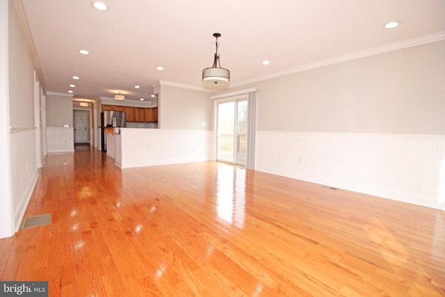 empty room with ornamental molding, light wood-style flooring, wainscoting, and visible vents