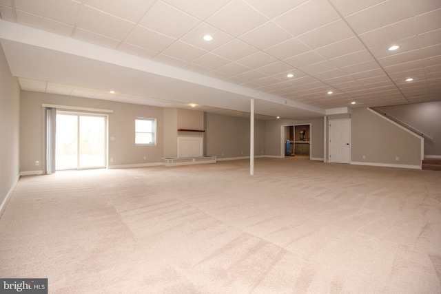 basement with a paneled ceiling, recessed lighting, light colored carpet, baseboards, and stairway