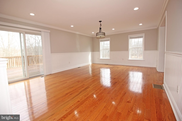 empty room featuring a wainscoted wall, crown molding, visible vents, and light wood-style floors