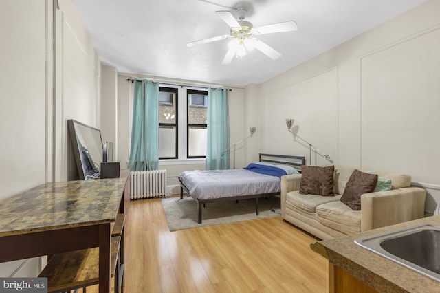 bedroom featuring light wood finished floors, radiator heating unit, a sink, and a ceiling fan