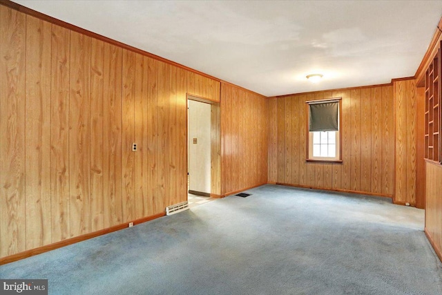 spare room featuring carpet floors, crown molding, visible vents, wood walls, and baseboards