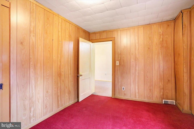 carpeted empty room featuring wood walls and visible vents