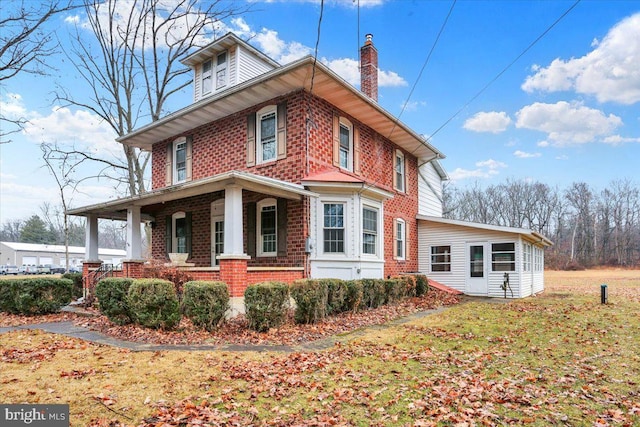 view of side of property with a porch, brick siding, and a chimney