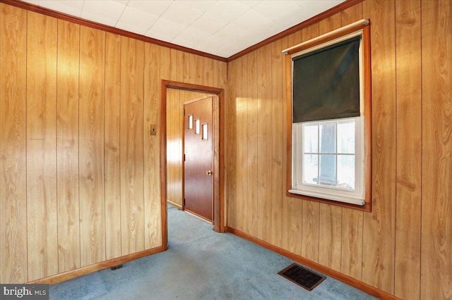 carpeted spare room featuring ornamental molding, visible vents, wood walls, and baseboards