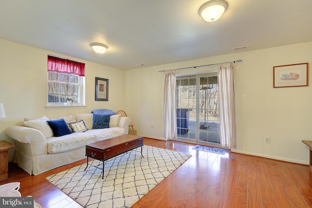 living area featuring baseboards, plenty of natural light, visible vents, and wood finished floors