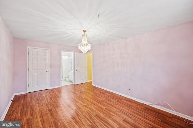 unfurnished room with an inviting chandelier, light wood-style flooring, and baseboards