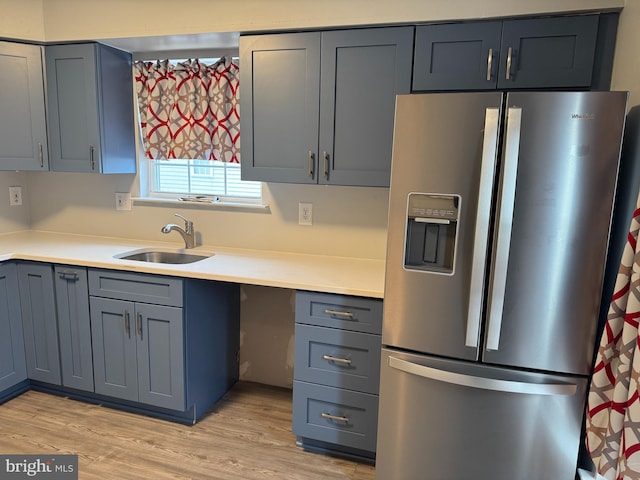 kitchen with light wood-style floors, light countertops, a sink, and stainless steel refrigerator with ice dispenser