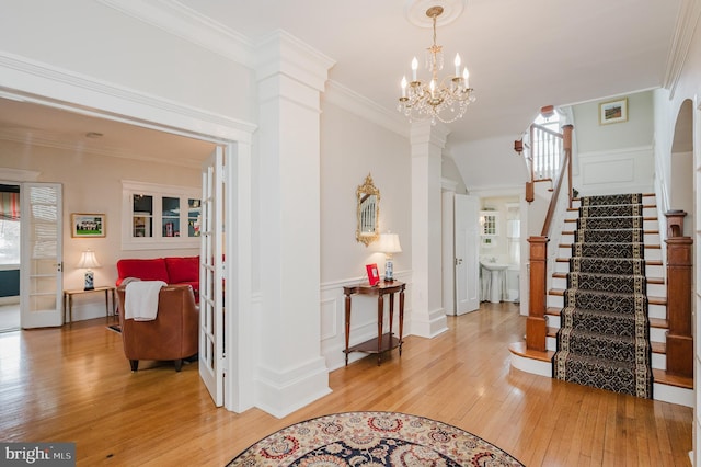 entryway with decorative columns, stairs, light wood-style floors, and crown molding