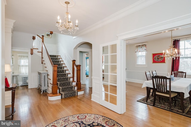 interior space with stairs, crown molding, light wood-style flooring, arched walkways, and an inviting chandelier