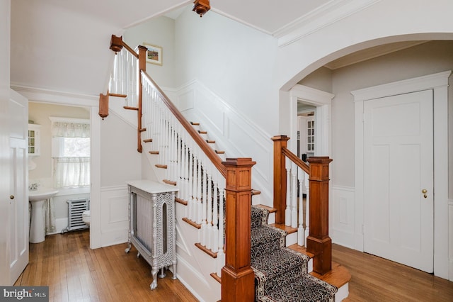 staircase with arched walkways, wainscoting, crown molding, and hardwood / wood-style floors