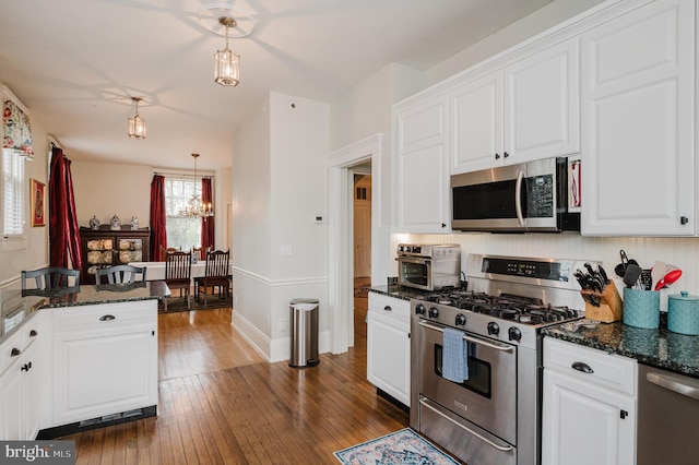 kitchen with white cabinetry, stainless steel appliances, dark stone countertops, dark wood-style floors, and a notable chandelier