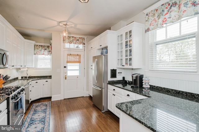 kitchen with white cabinetry, appliances with stainless steel finishes, glass insert cabinets, dark wood-type flooring, and dark stone counters